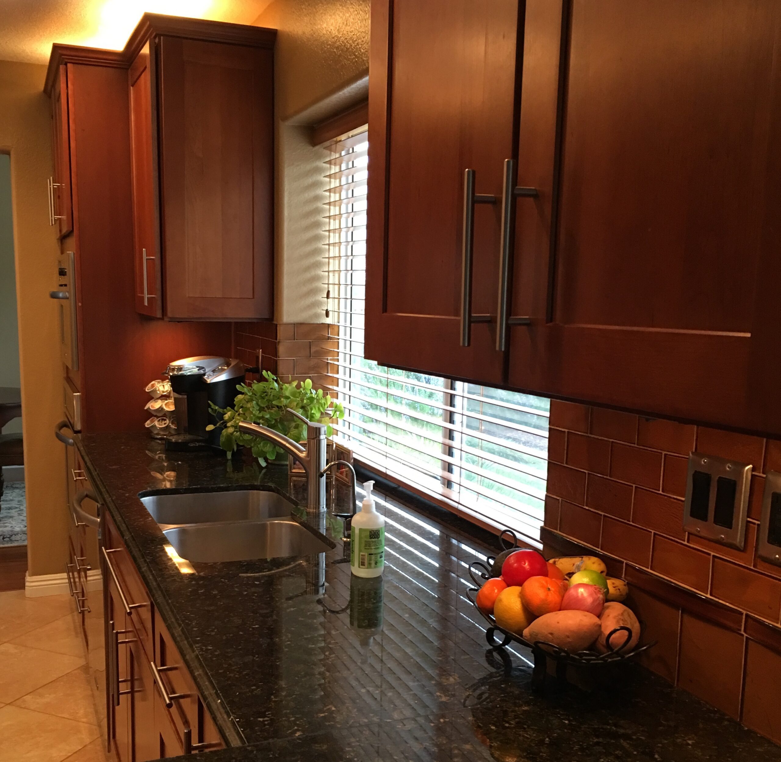 A well-lit kitchen corner with wooden cabinets, stainless steel appliances, and a bowl of fruit on the counter.
